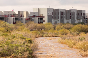 Obraz premium Brown water after heavy rains flows by apartment buildings next to river on sunny day