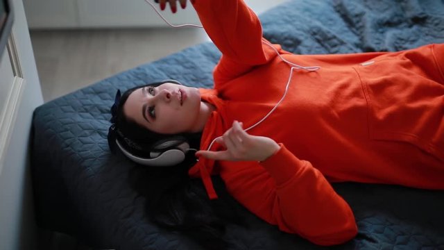 Young sexy girl talks by smartphone, online video chatting, communicate with friend lying at home bed