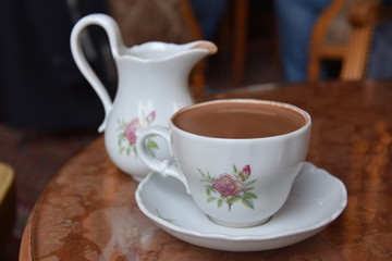 cup of hot chocolate with teapot  on wooden table