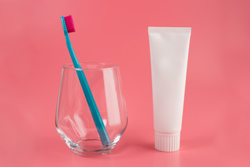 Toothbrush in glass isolated on pink background with toothpaste tube