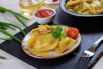 Traditional Italian homemade ravioli pasta stuffed with potatoes and spinach with tomato sauce, olive oil and basil on a black stone board