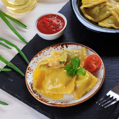 Traditional Italian homemade ravioli pasta stuffed with potatoes and spinach with tomato sauce, olive oil and basil on a black stone board