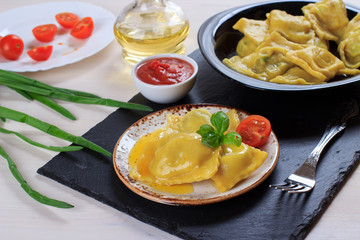 Traditional Italian homemade ravioli pasta stuffed with potatoes and spinach with tomato sauce, olive oil and basil on a black stone board