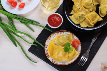 Traditional Italian homemade ravioli pasta stuffed with potatoes and spinach with tomato sauce, olive oil and basil on a black stone board
