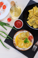 Traditional Italian homemade ravioli pasta stuffed with potatoes and spinach with tomato sauce, olive oil and basil on a black stone board
