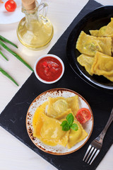 Traditional Italian homemade ravioli pasta stuffed with potatoes and spinach with tomato sauce, olive oil and basil on a black stone board