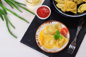 Traditional Italian homemade ravioli pasta stuffed with potatoes and spinach with tomato sauce, olive oil and basil on a black stone board