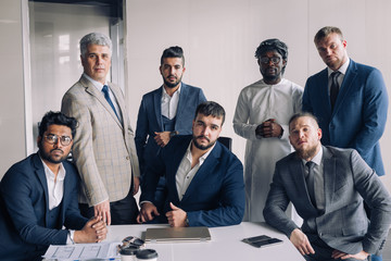 Diverse serious business men gather at conference table together with his caucasian athletic young boss, attending meeting or corporate briefing. African, indian businessmen partners team.