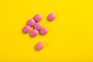 Assorted pharmaceutical medicine pills, tablets and capsules. Yellow background.