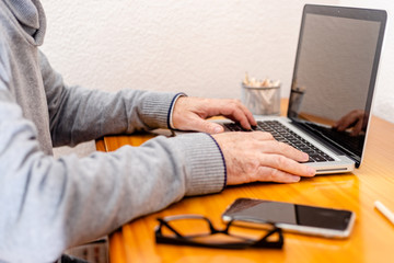 Close up low angle view of a man working from home on a laptop computer sitting at a desk surfing the internet.