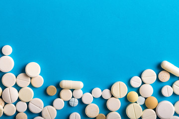 Assorted pharmaceutical medicine pills, tablets and capsules. Blue background.