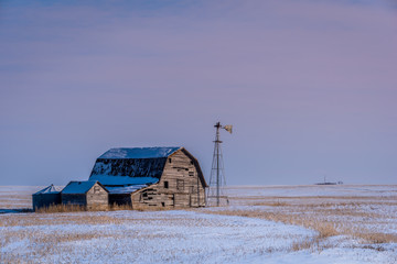 Vintage barn, bins and windmill surrounded by snow under a pink sunset sky in Saskatchewan 