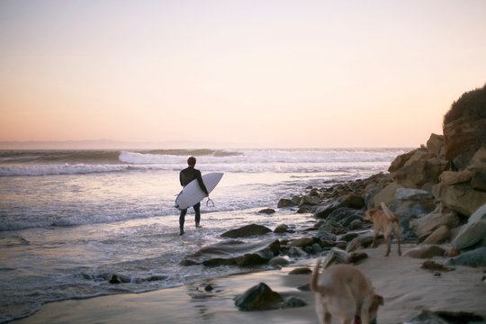 Man walking along coastline carrying surfboard 