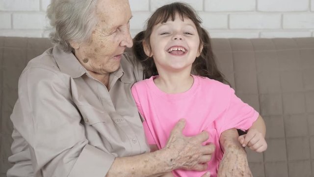 Grandmother tickles a granddaughter. A happy little girl is tickled by an old granny.