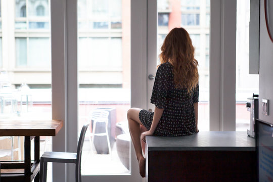 Young woman sitting on counter in kitchen and looking through window 
