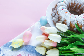 Happy Easter! Big plate with cake and hand painted colorful eggs, tulips and cup of coffee on pink background. Close up. Decoration for Easter, festive background.