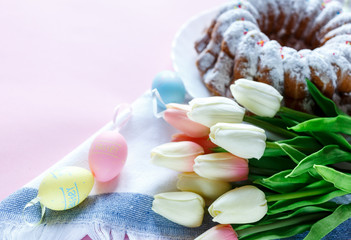 Happy Easter! Big plate with cake and hand painted colorful eggs, tulips and cup of coffee on pink background. Close up. Decoration for Easter, festive background.