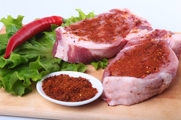 Raw pork steak with herbs, chili pepper and spices on cutting board. Ready for bbq.