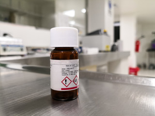 Hazardous chemical in an amber bottle with light protection on top of an aluminum laboratory bench