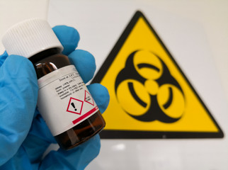 Concept of hazardous material or harmful chemical reagent. Hand with a protective glove holding an...