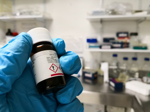 Chemical Reagent In A Black Bottle With A Hazard Label. Hand Of A Scientist In A Laboratory.
