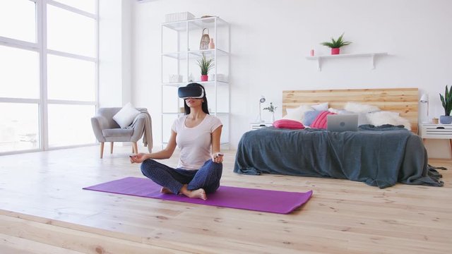 Young female doing yoga in VR glasses at home