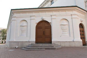 wooden arched brown doors in a white building with stucco on the wall