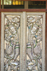 Beautiful silver door leaves with carved silver angels image. Thai style patterned on door leaves made of silver and glass with angels image. Public temple in Chiang Mai, Thailand.