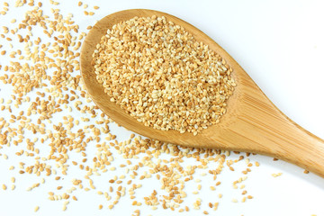 Sesame seeds in wooden spoon isolated on white background, top view.