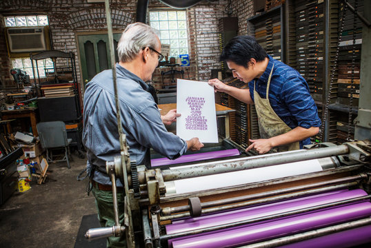 Workers holding freshly printed sheet of paper 