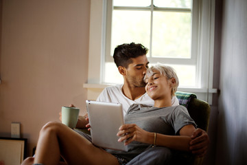 Young couple sitting in armchair using tablet pc 