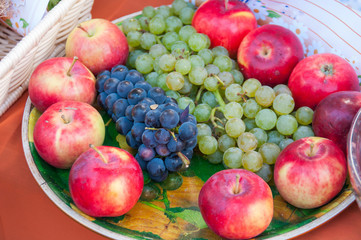 Autumn harvest: fruit on a plate, red apples, green and black grapes