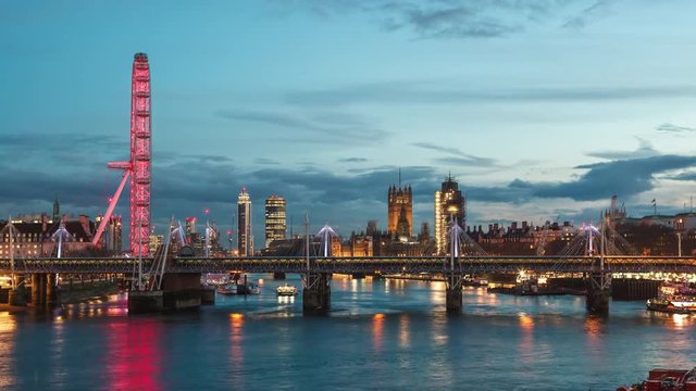 London time-lapse after sunset, blue hour on the Thames. Hungerford Bridge and the Big Ben with the London Eye in the view.