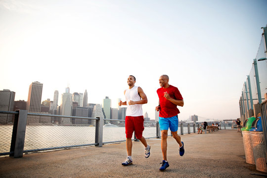 Two men running along waterfront cityscape in background 