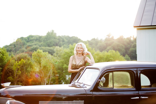 Glamorous mature woman posing behind vintage car 