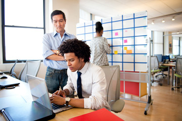 Boss looking over employee's shoulder in office 