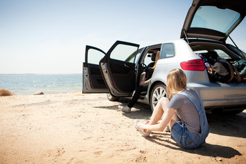 Young woman sitting next to car and tying shoes on beach 