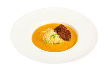 White plate with yellow vegetable cream soup with cheese and dried tomatoes.