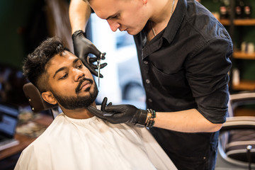Barber styling beard with scissors at barbershop. Stylish hairdresser in male hair salon