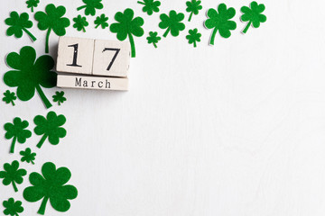 Block calendar for St Patrick's Day, March 17, with green clover leaf, green water and paper tag on white wooden background