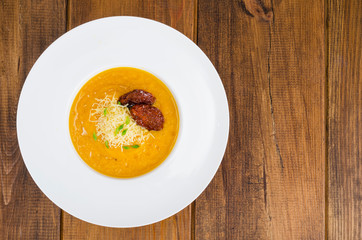 Plate with pumpkin crem soup and dried tomatoes on wooden background