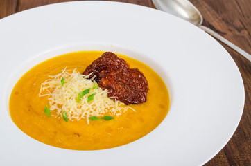 Plate with pumpkin crem soup and dried tomatoes on wooden background