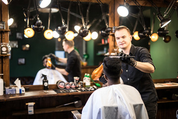 Barber with hairdryer drying and styling hair of client. Barber with hairdryer works on hairstyle for bearded man, barbershop background. Styling concept. Hipster bearded client getting hairstyle.