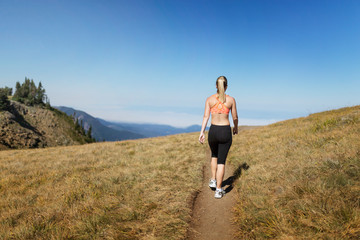 Rear view of young woman in sportswear walking along trail in mountains 
