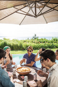 Young people playing cards at table by poolside 