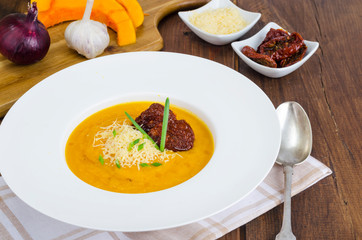 Plate with pumpkin crem soup and dried tomatoes on wooden background