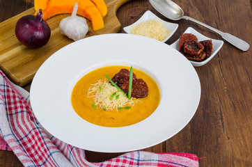 Plate with pumpkin crem soup and dried tomatoes on wooden background