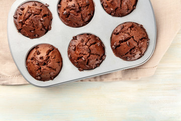 A closeup photo of chocolate chip muffins in a baking mould, shot from the top on a light background with a place for text