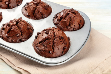 A closeup photo of chocolate chip muffins in a pan on a light background