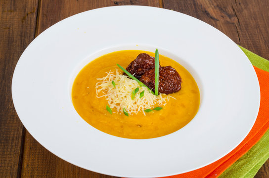 Plate with pumpkin crem soup and dried tomatoes on wooden background